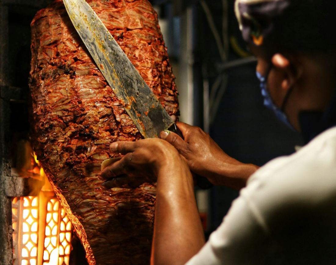 Cook slicing al pastor meat from a spit