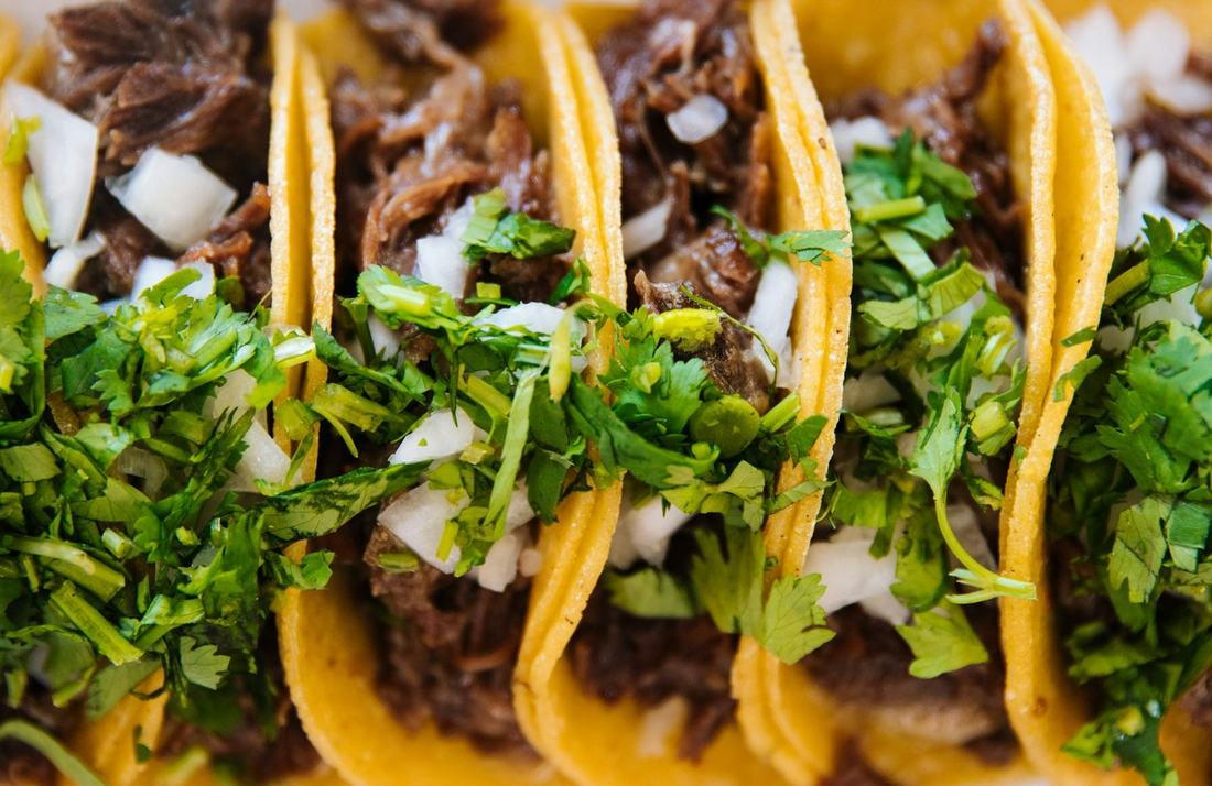 Row of street tacos topped with cilantro and onion