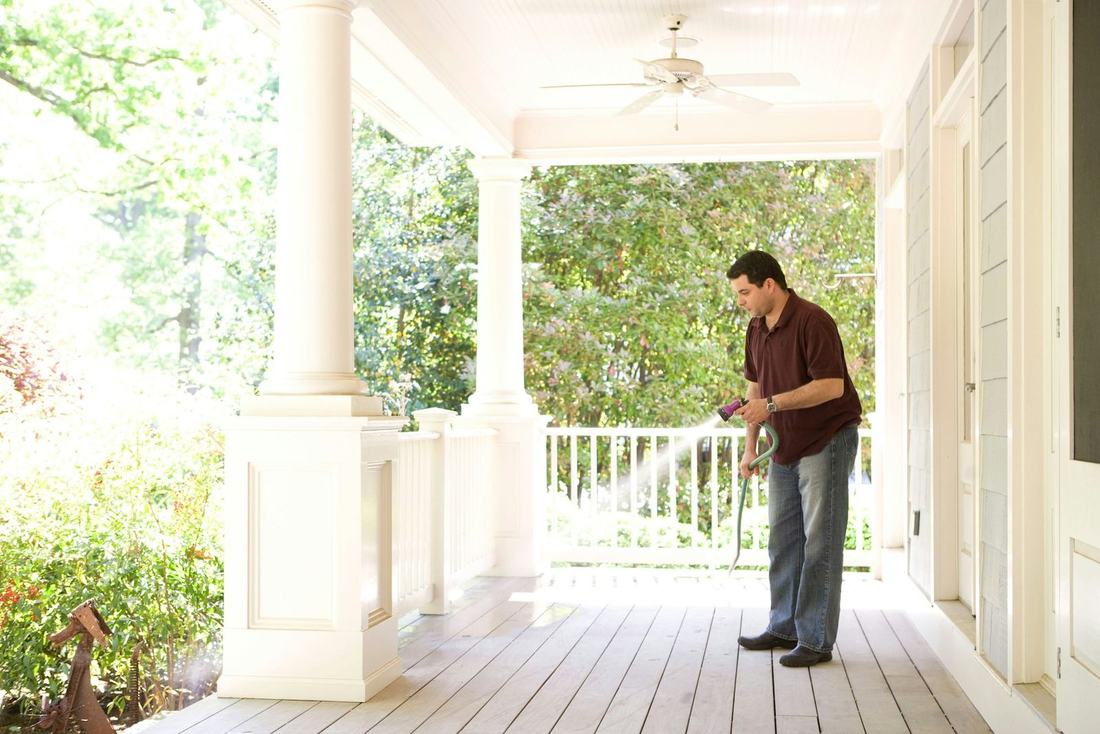 Man spraying a treatment along a covered front porch
